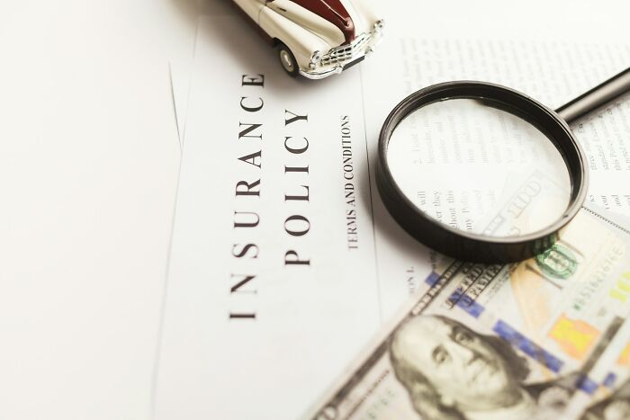 Magnifying glass on insurance policy with toy car and dollar bill, illustrating people and boring industries concept.