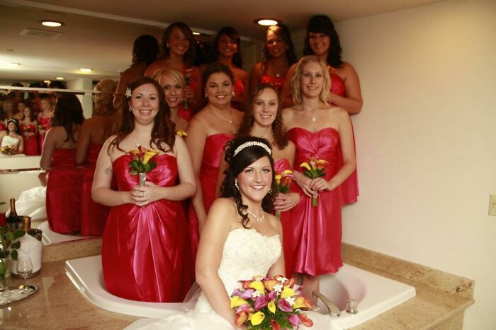 Bride and bridesmaids in red dresses posing awkwardly in a bathroom setting for awkward wedding photos.