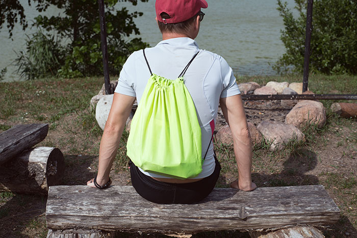 Man wearing red cap and neon green backpack sitting on a wooden bench near a lake, reflecting on attraction moments and ick feelings.