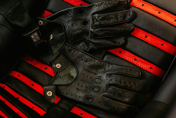 Black leather driving gloves resting on a vintage car seat with red and black striped upholstery, illustrating weird ick attraction.