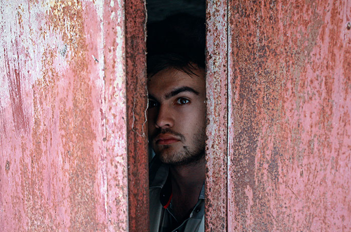 Man snooping on his wife's conversation with her sister, looking shocked and devastated behind a rusty door.