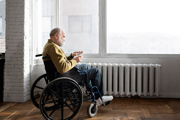 Elderly man in wheelchair sitting by window holding a glass, reflecting on complaints about sister-in-law stay.