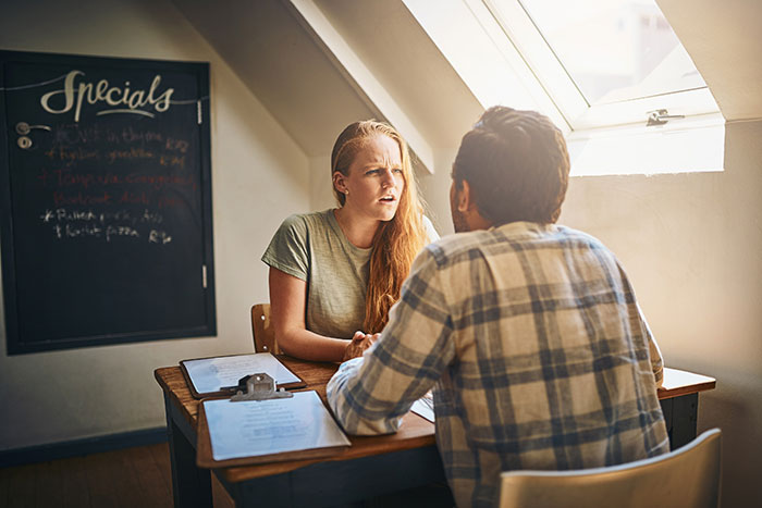Woman looking frustrated while talking to husband at a table, illustrating complaints about SIL despite free stay.