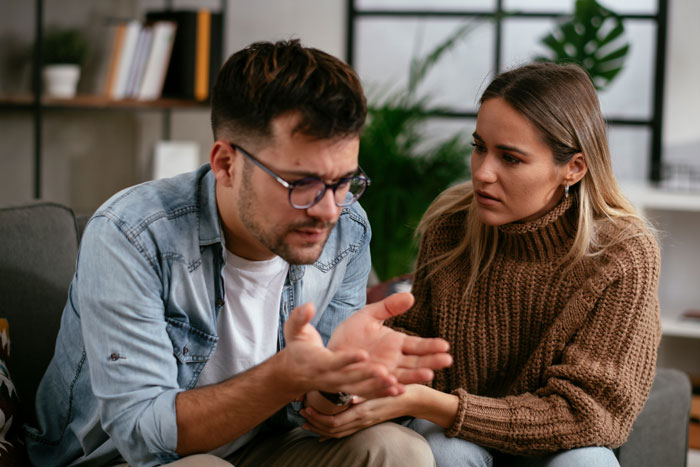 Man suspects wife on couch, distressed man and concerned woman in tense relationship conversation