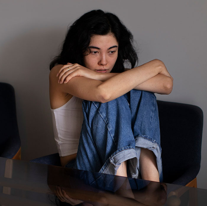 Woman sitting alone at home, wearing casual clothes, showing discomfort related to not wearing a bra around husband.