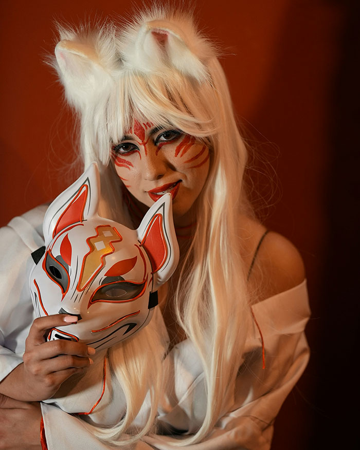 Person in cosplay with white hair, fox ears, and painted face holding a fox mask, capturing a weird and unexplained moment.