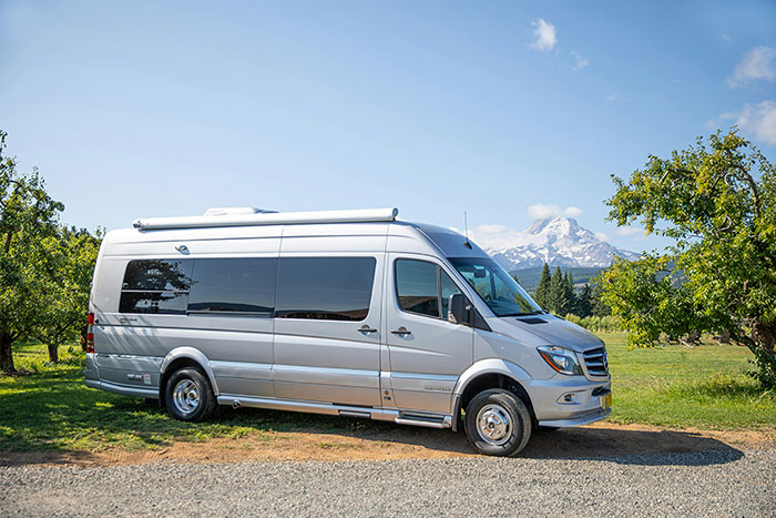 Silver camper van parked on a rural road with trees and a mountain in the background, capturing something weird witnessed outdoors.