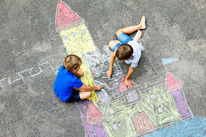 Two children drawing a colorful chalk castle on pavement, showcasing a weird and unexplained outdoor activity.