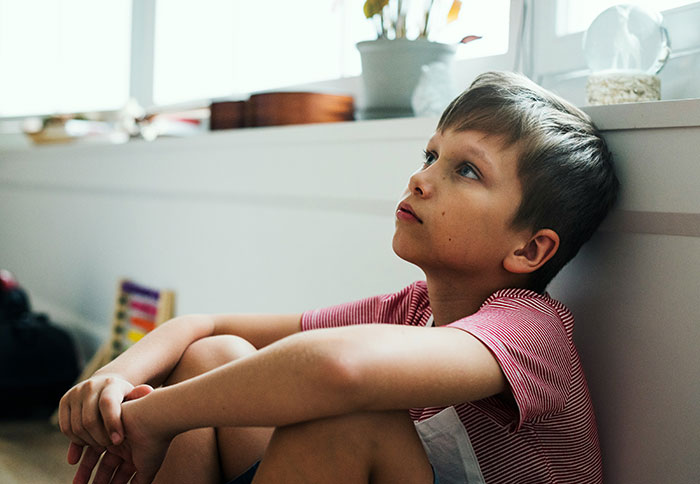 Young boy sitting on the floor looking puzzled and thoughtful after witnessing something weird he can’t explain.
