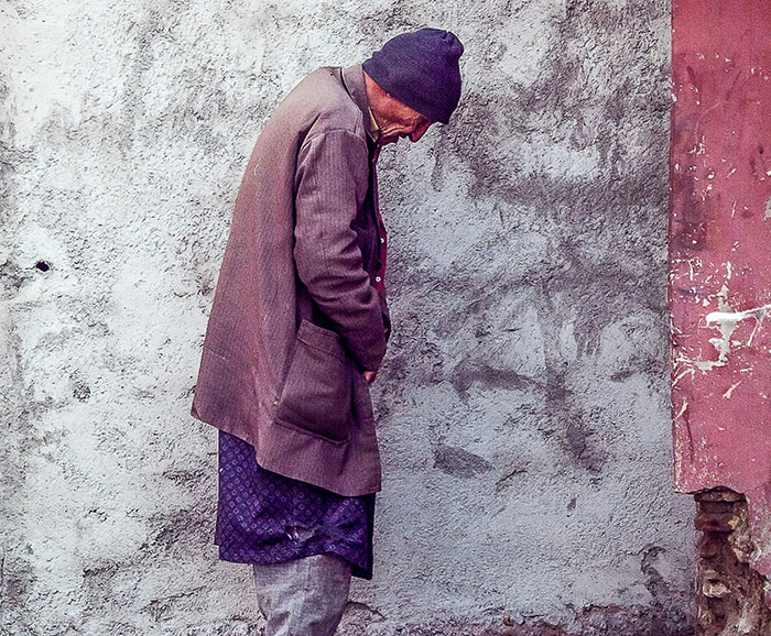 Man wearing a purple coat and hat standing against a rough wall, evoking a scene people witnessed that’s still unexplained