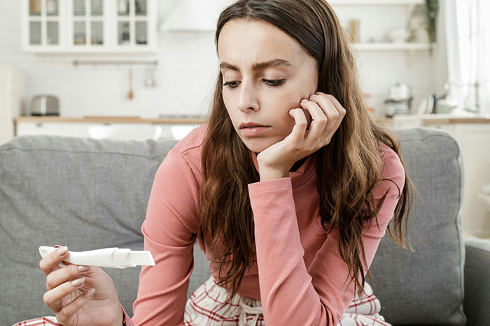 Young woman looking worried while holding a pregnancy test, reflecting distress over 25-year-old mom trapped with partner.
