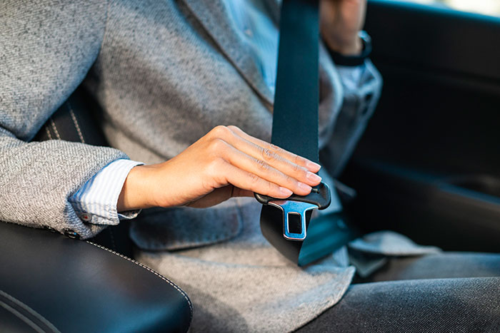 Woman fastening seat belt in car, emphasizing safety and refusal to drive until all friends buckle up during road trip.