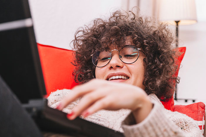 Woman with curly hair and glasses smiling while using a laptop, highlighting seat belt safety on a road trip.