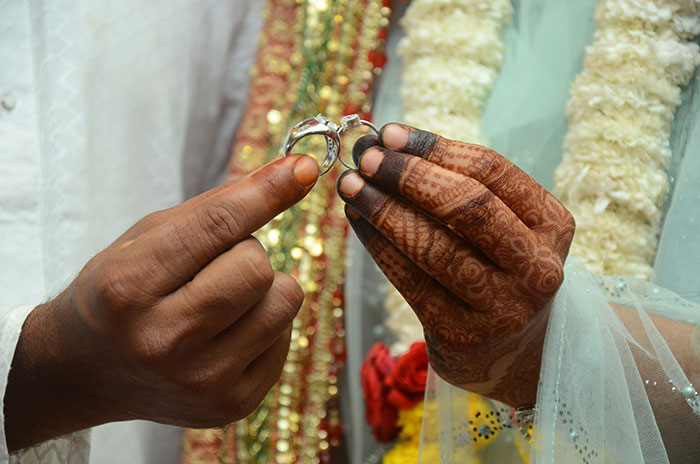 Close-up of hands with henna holding wedding rings during an arranged marriage proposal ceremony in India.