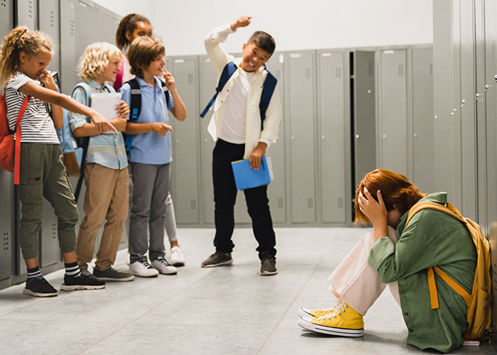 Group of school children bullying a girl in a hallway, highlighting obsession with bully affecting relationships and stalking behavior.