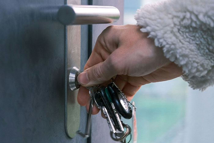 Hand holding keys unlocking an apartment door, representing a man noticing strange things happening inside. Hand holding keys unlocking an apartment door, representing a man noticing strange things happening inside.
