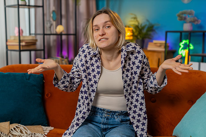 Annoyed woman shrugging on couch about a heated blanket gift in a colorful living room Annoyed woman shrugging on couch about a heated blanket gift in a colorful living room