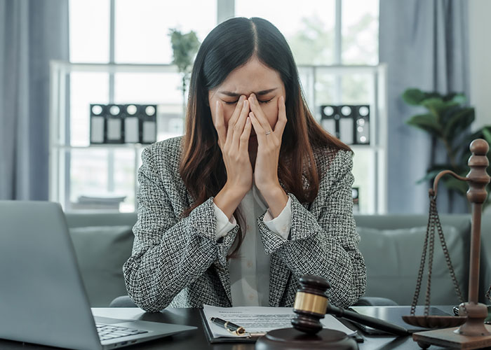 Woman in career attire stressed at desk with legal documents, laptop, and scale symbolizing career challenges and true colors revealed.
