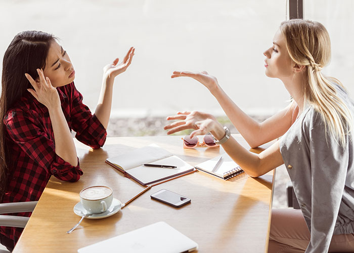 Two women in a heated discussion at a cafe, highlighting a woman protecting her new career from free advice.