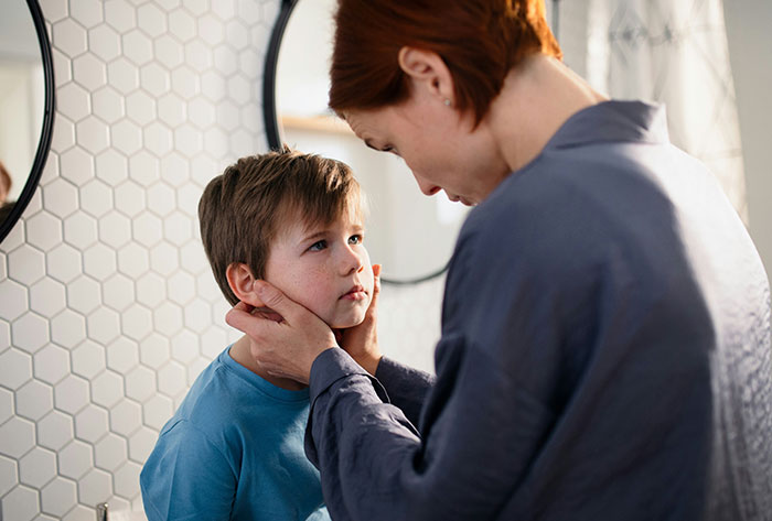 Woman gently holding a young boy’s face in a bathroom, illustrating a man torn between husband and mother-in-law.