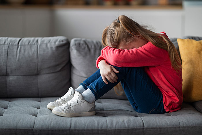 Sad young girl in red sweater sitting on couch with head resting on arms, reflecting on family conflict and trip to Italy.