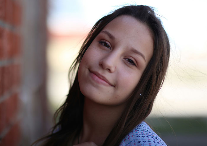 Young woman smiling gently outdoors with blurred background, illustrating what women obsess over for no reason at all.