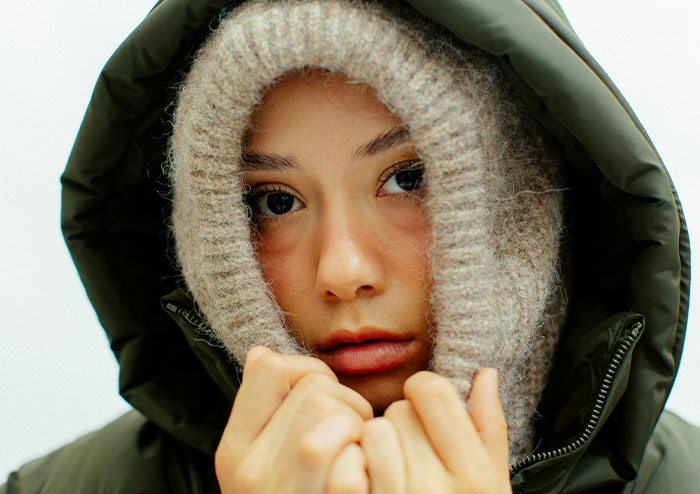 Young woman in a green jacket and knitted hood looking at the camera, representing what women obsess over for no reason.