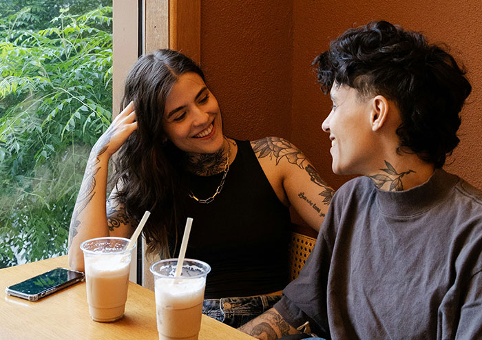 Two people with tattoos smiling and talking over iced coffee, illustrating what women obsess over according to men’s views.