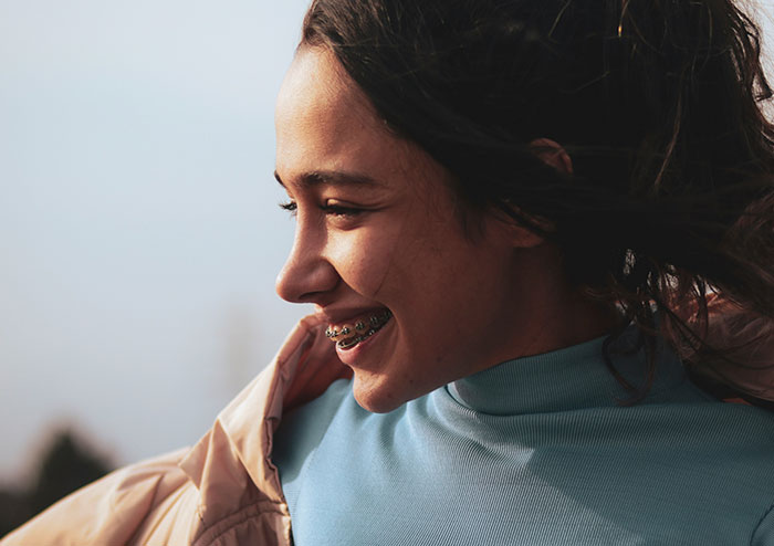 Young woman smiling outdoors with braces, capturing what women obsess over for no reason according to men’s perspective.