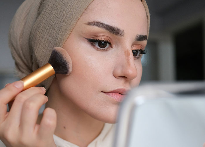 Young woman applying makeup with a brush, illustrating what women obsess over for no reason at all according to men.