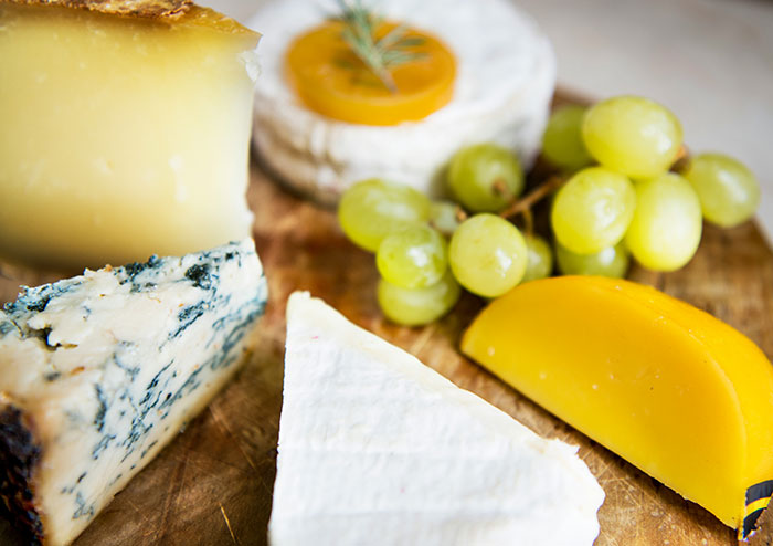 Variety of gourmet cheeses and grapes on wooden board, illustrating what women obsess over for no reason.