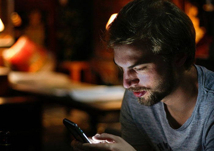 Young man using smartphone in low light, reflecting on what women obsess over as shared by 48 men online.