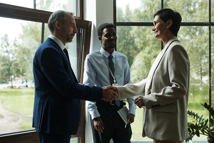 Businesswoman and businessman shaking hands in an office setting with a colleague discussing misconceptions about women and men.