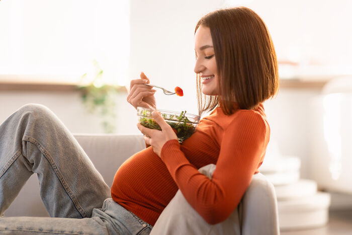 Pregnant woman in orange sweater enjoying a healthy salad, challenging common misconceptions about women today.
