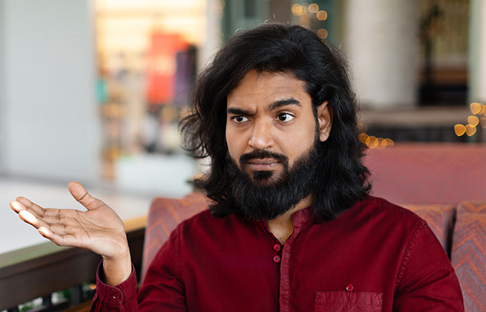 Man with beard and long hair wearing a red shirt, gesturing with confusion, illustrating servers sharing customer horror stories.
