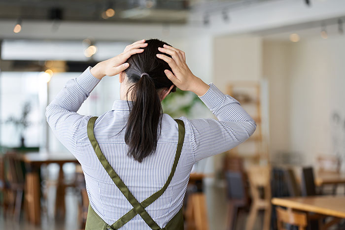 Restaurant server in apron with hands on head showing stress in a busy dining area illustrating customer horror stories.
