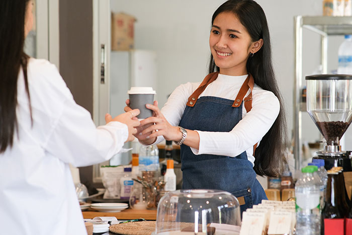Smiling server handing coffee to customer in cafe as servers share customer horror stories and true nightmares.