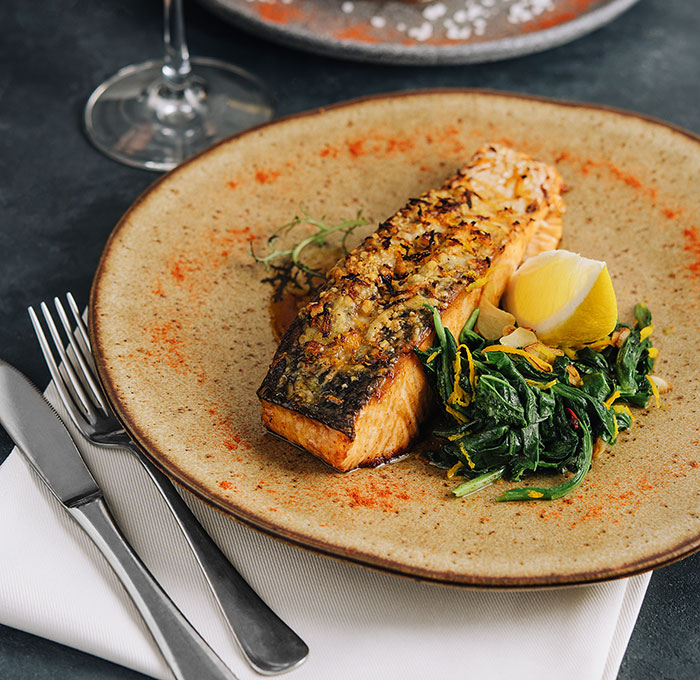 Grilled salmon dish served with sautéed greens and lemon wedge on a plate, illustrating servers sharing customer horror stories.