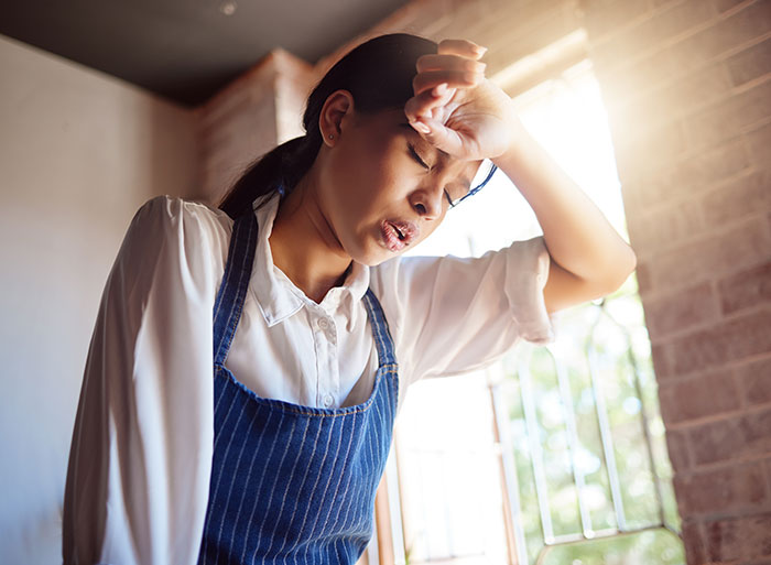 Stressed female server wiping sweat from forehead after dealing with difficult customers in a busy restaurant setting.