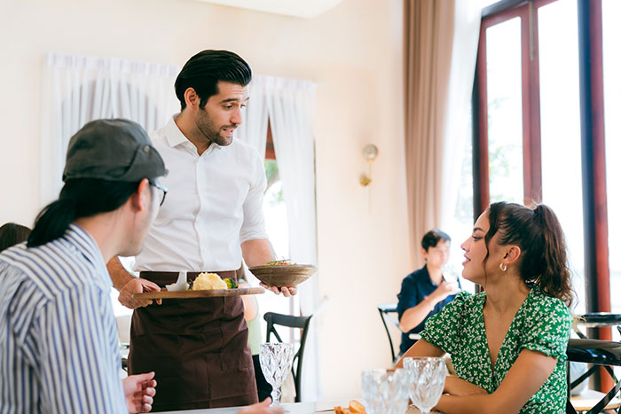 A server interacts with customers while holding plates, illustrating servers sharing customer horror stories.