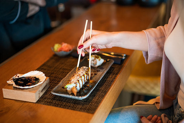 Person using chopsticks to pick up sushi on a plate at a restaurant, illustrating servers sharing customer horror stories.