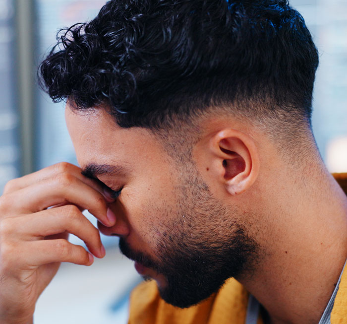 Man with beard and curly hair pinching the bridge of his nose, appearing stressed by customer horror stories shared by servers.