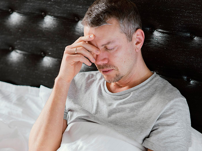 Man sitting in bed with hand on forehead, appearing distressed by heartbreaking medical conditions that can't be cured