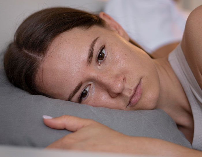 Young woman lying down looking sad and tired, illustrating the emotional impact of heartbreaking medical conditions.