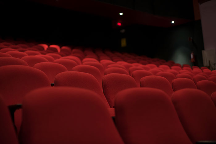 Empty red theater seats in a dark auditorium representing lucky times people escaped dangerous situations unseen.