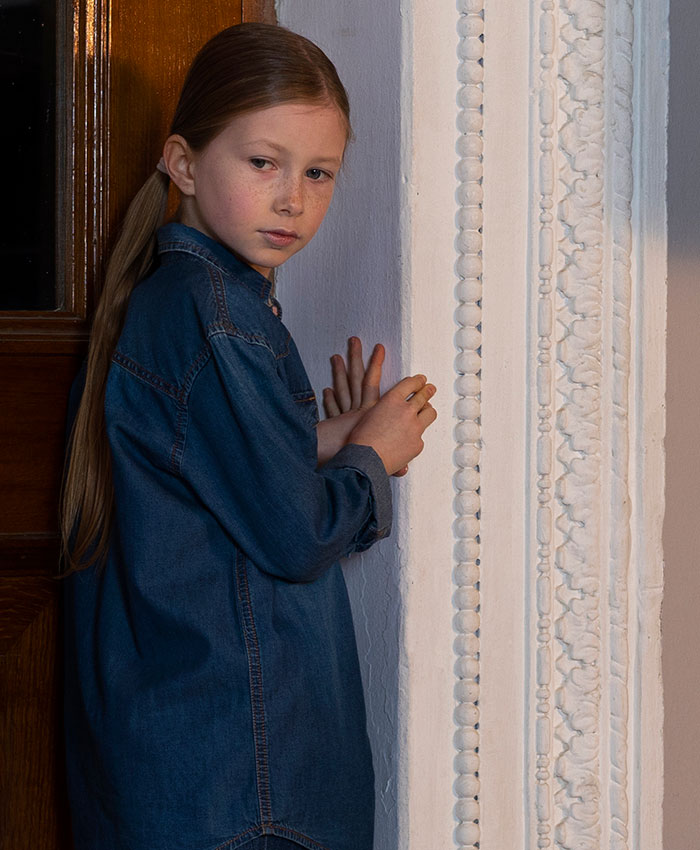 Young girl in a denim jacket cautiously peeking around a decorated corner, capturing lucky moments of escape.