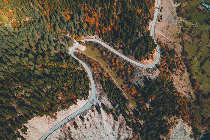 Aerial view of a winding mountain road surrounded by dense forest and rocky terrain, highlighting close calls nature.