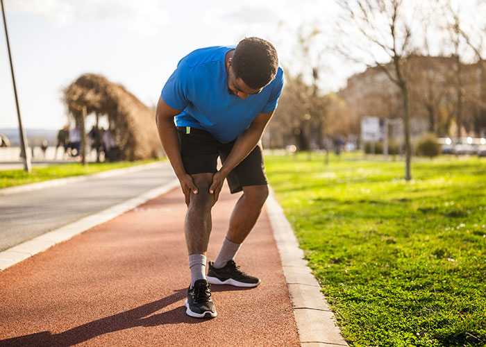 Man in blue shirt clutching knee on running path, illustrating moments when people were in the wrong place at the wrong time.
