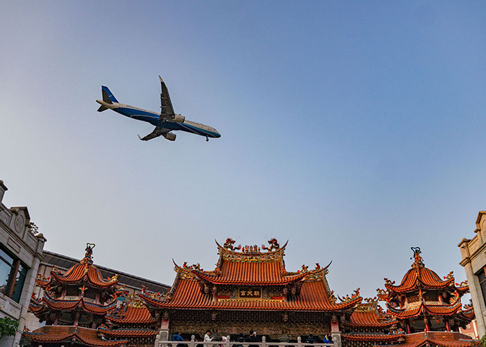 Airplane flying low over traditional Asian temple, capturing a moment of being in the wrong place at the wrong time.
