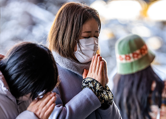 Three people wearing face masks praying closely together, capturing a moment of people in the wrong place at the wrong time.